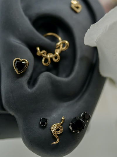 black and gold heart tragus piercing, black prong set neometal ends, texturd snake by junipurr in ear lobes with kaa daith piercing hoop 