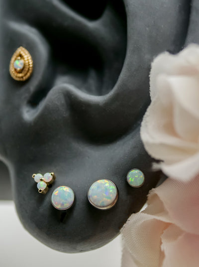 ear piercing on lobe, opal trinity by junipurr, and tragus piercing pear shape yellow gold by junipurr and bezel set flat opal threadless ends in lobes